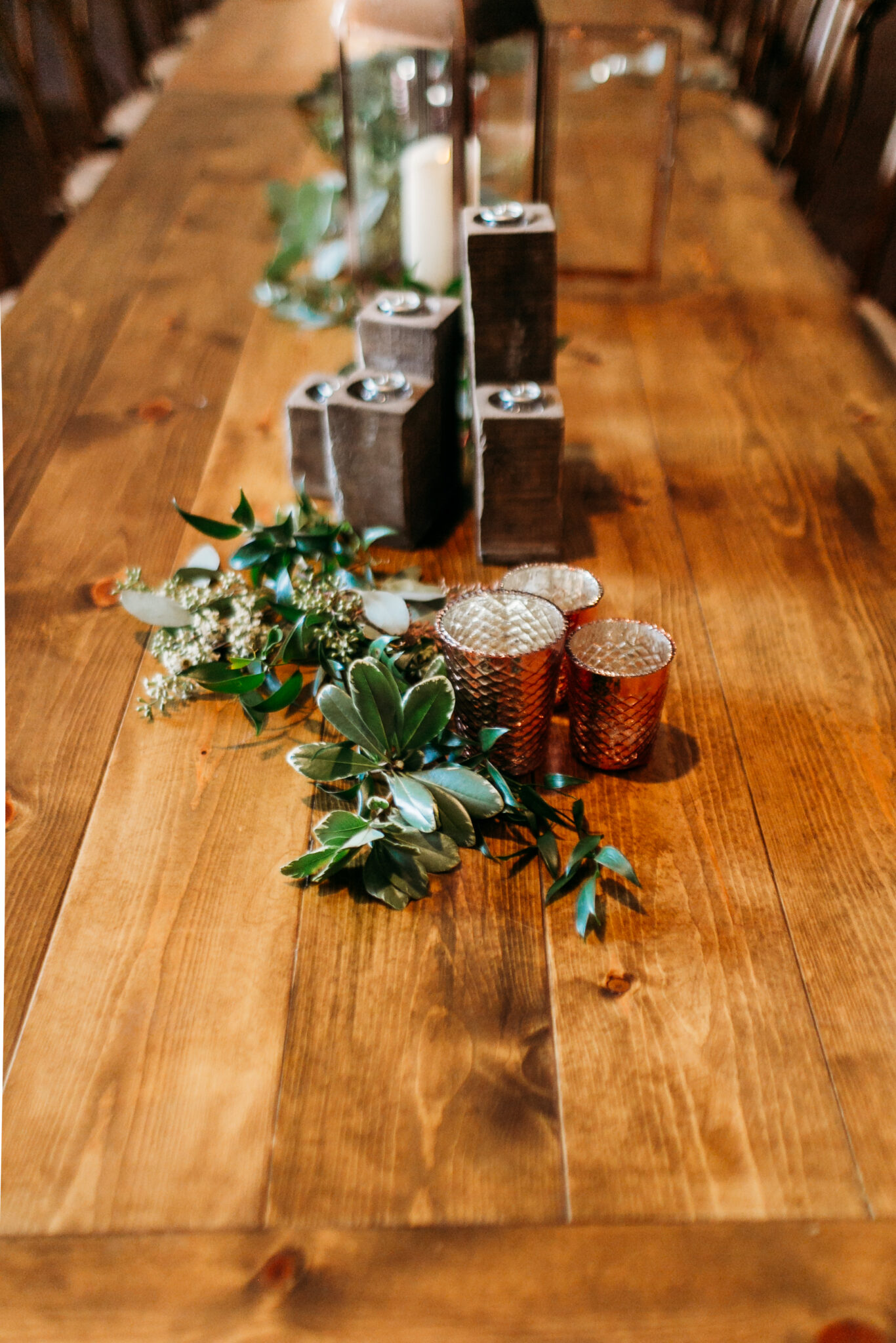 Candles, candle holders, and decorative leaves on top of a wood long table