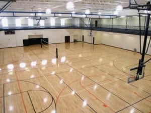 Shiny wooden gymnasium floor with a basketball ring and a volleyball net